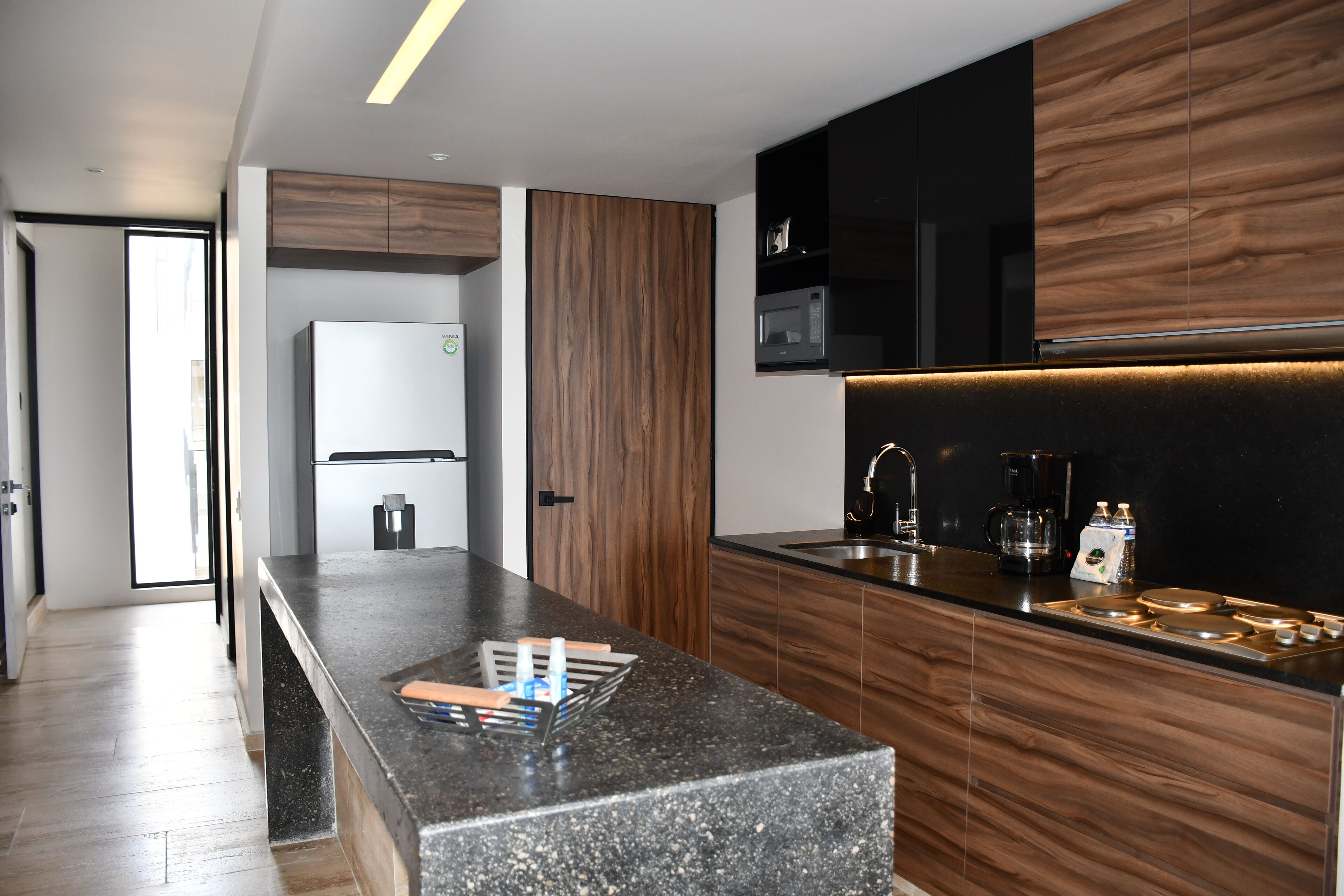 A modern kitchen with a granite countertop, wooden cabinets, a built-in microwave, and a coffee maker.
