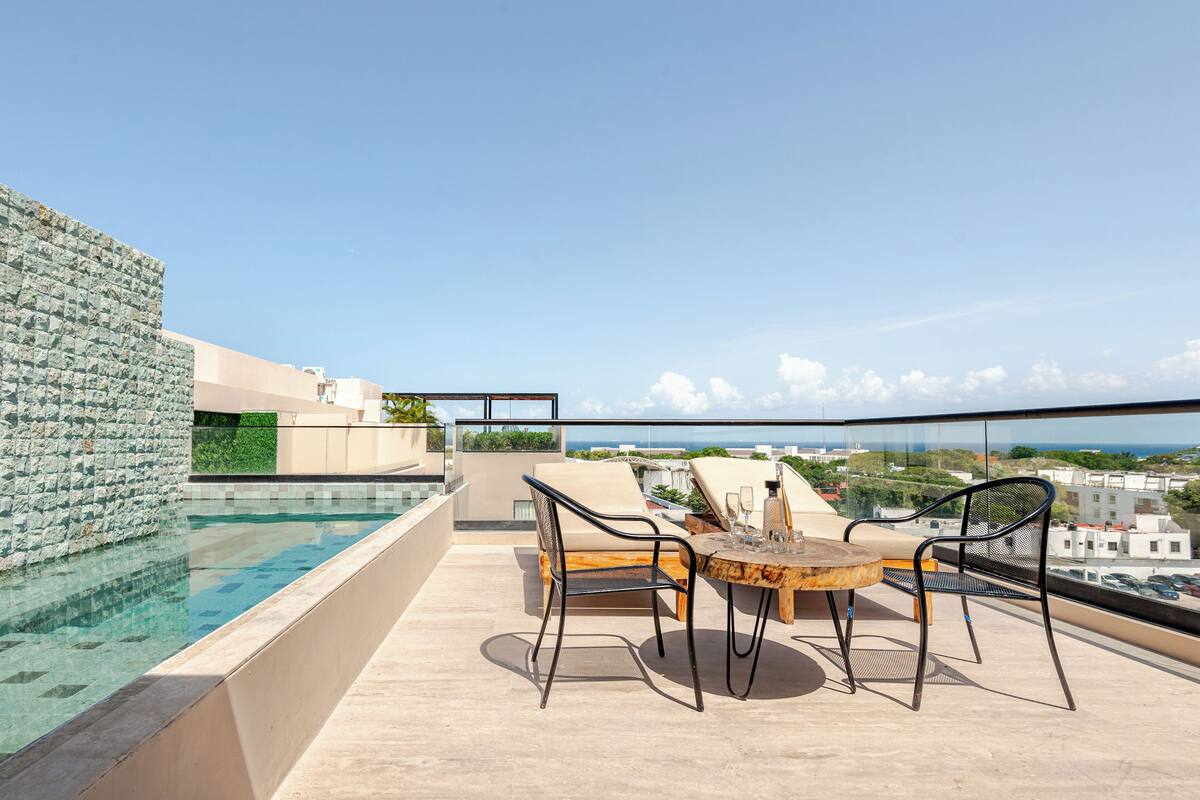 Une terrasse sur le toit avec une piscine, des chaises longues et une table.
