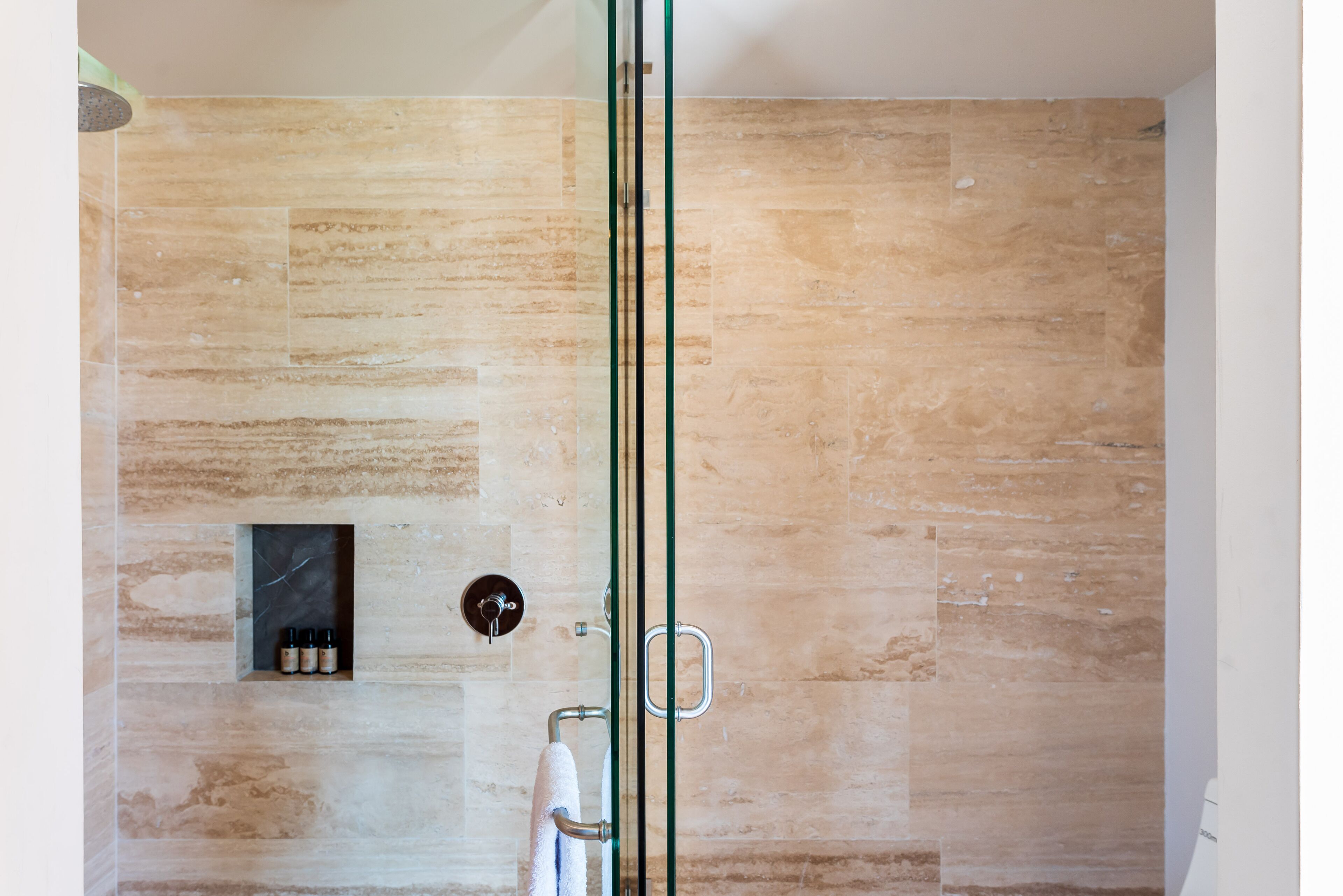 Une douche moderne avec une porte en verre, un porte-serviettes et une étagère pour les articles de toilette.