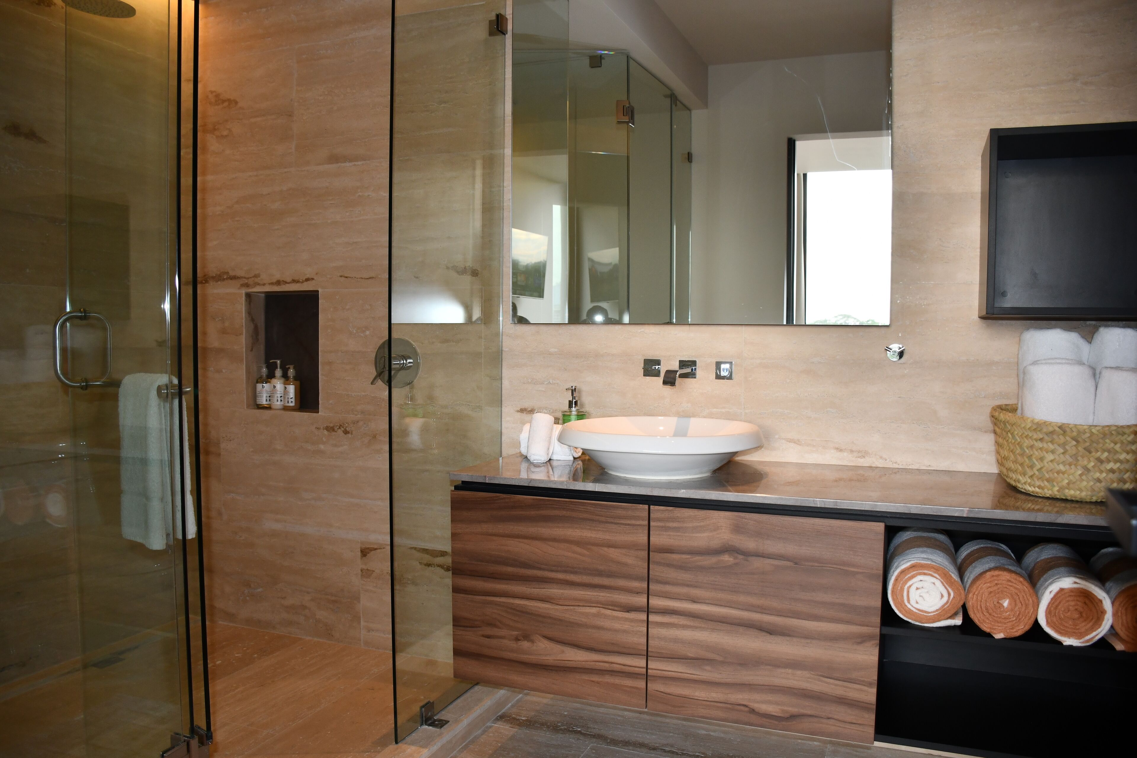 Een moderne badkamer met een douchecabine van glas, een houten wastafelmeubel en een grote spiegel.
