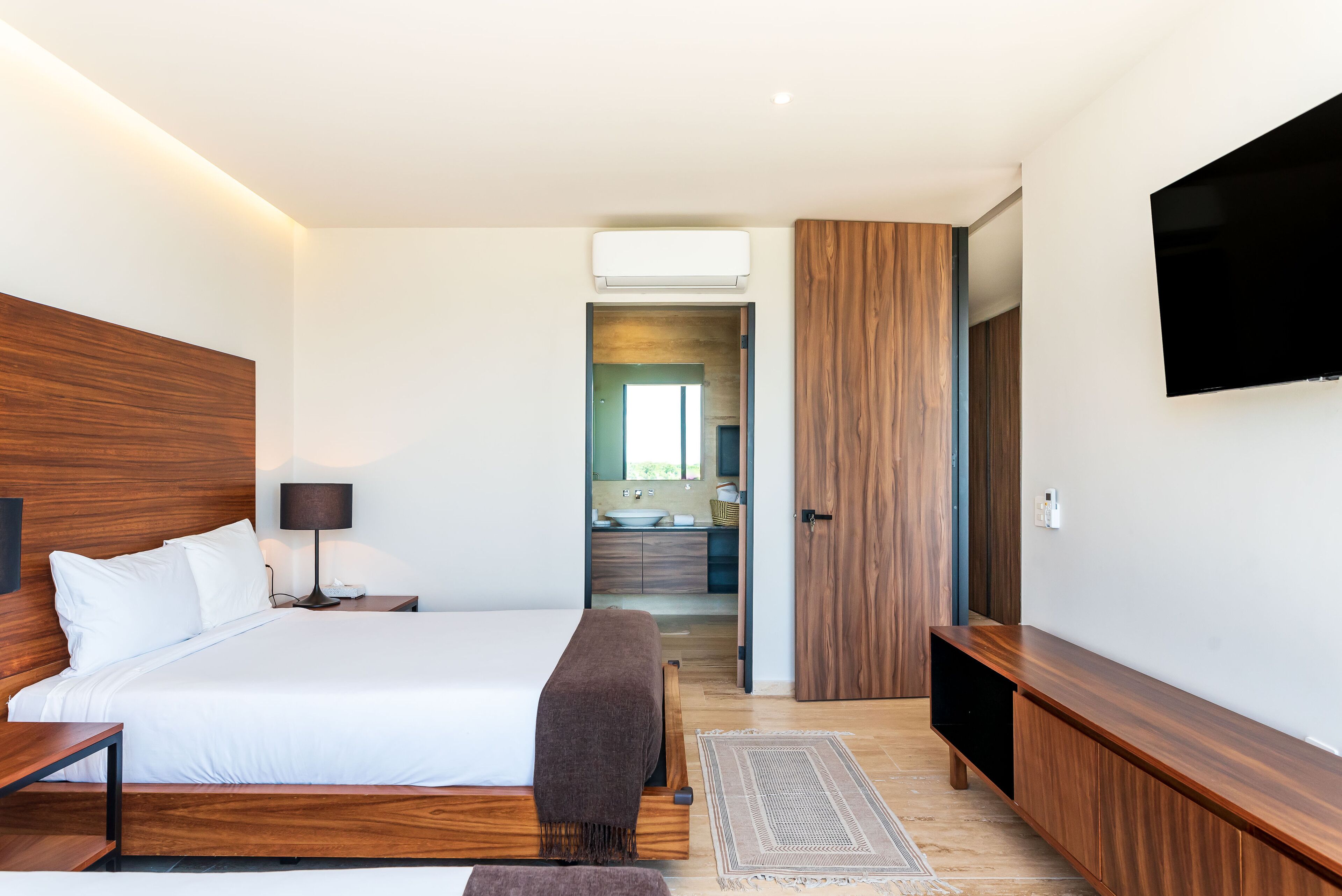 A modern bedroom with a large bed, bedside tables, a TV, and a walk-in closet.