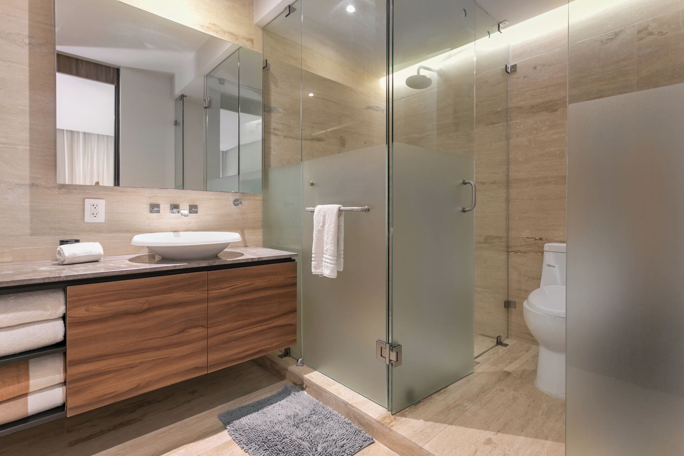 Un baño moderno con ducha de vidrio, tocador de madera y un espejo grande.