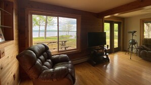 A wooden cabin interior with a leather sofa, a television, and a telescope.