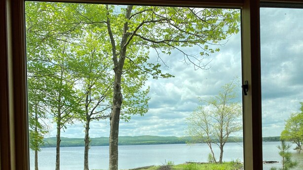 A wooden deck with a picnic table, a view of a lake, and trees in the background.