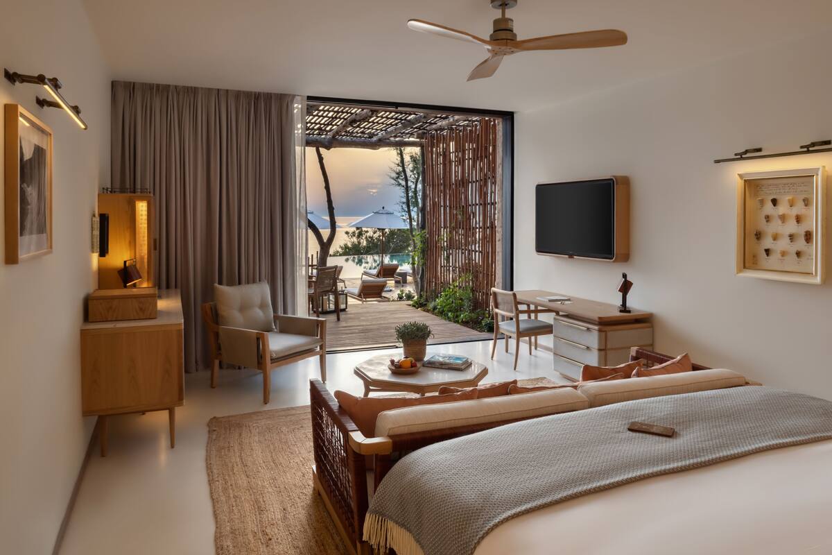 Een moderne hotelkamer met een groot bed, een bureau, een stoel en een balkon met zitplaatsen buiten.