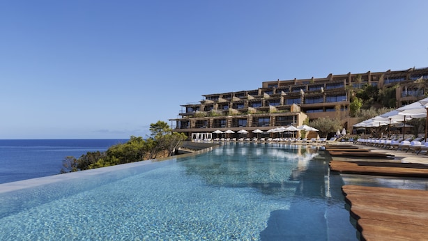 An infinity pool with clear blue water, wooden deck, and lounge chairs, overlooking the ocean and a multi-story hotel building. - Six Senses Ibiza (Sant Joan de Labritja)