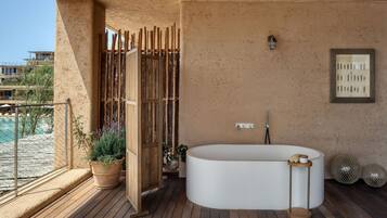 A modern bathroom with a freestanding bathtub, a wooden door, and a potted plant.
