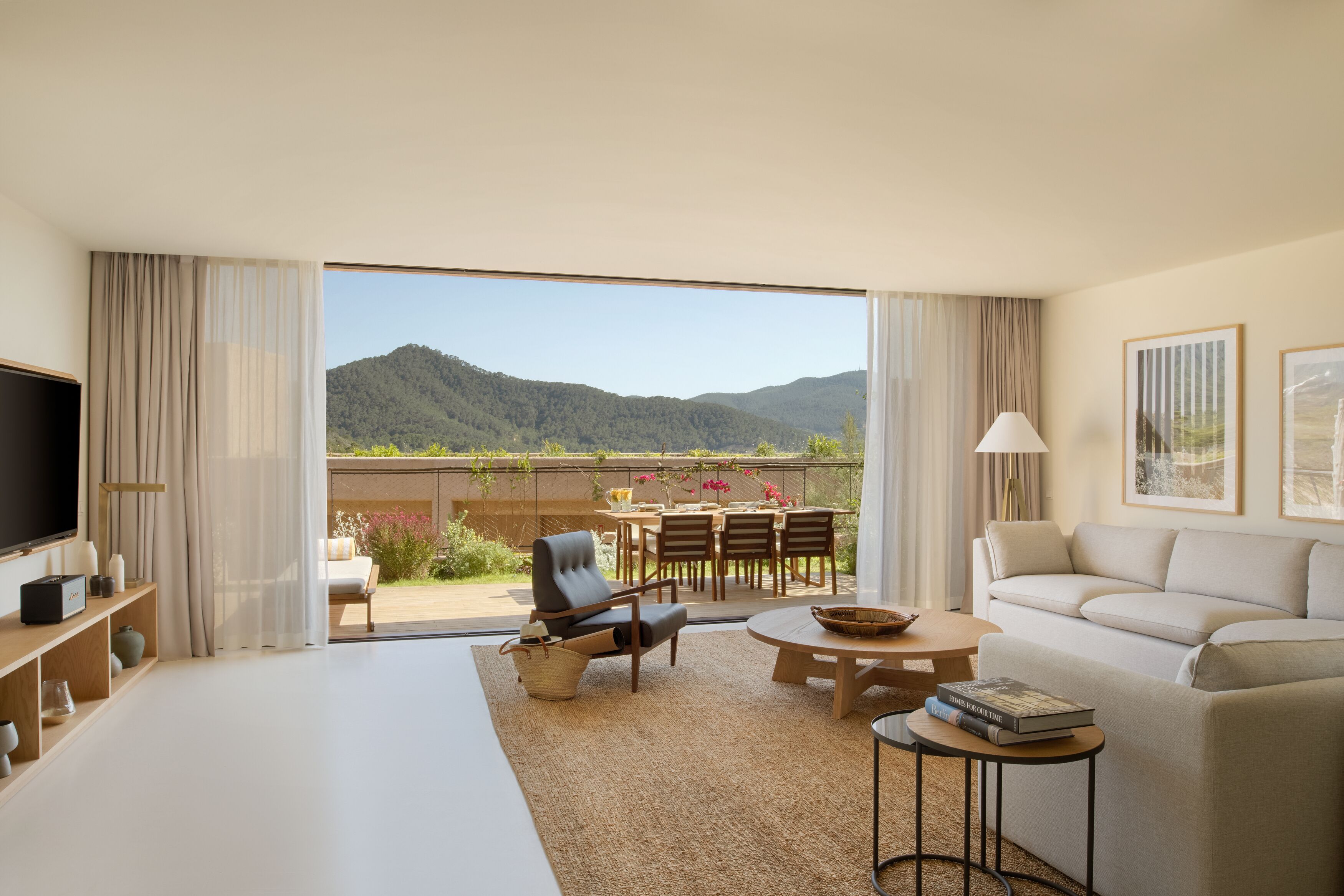 Une chambre d’hôtel moderne dotée d’un grand lit, d’une télévision, d’un canapé, d’un coin repas avec une table et des chaises, et offrant une vue sur les montagnes.