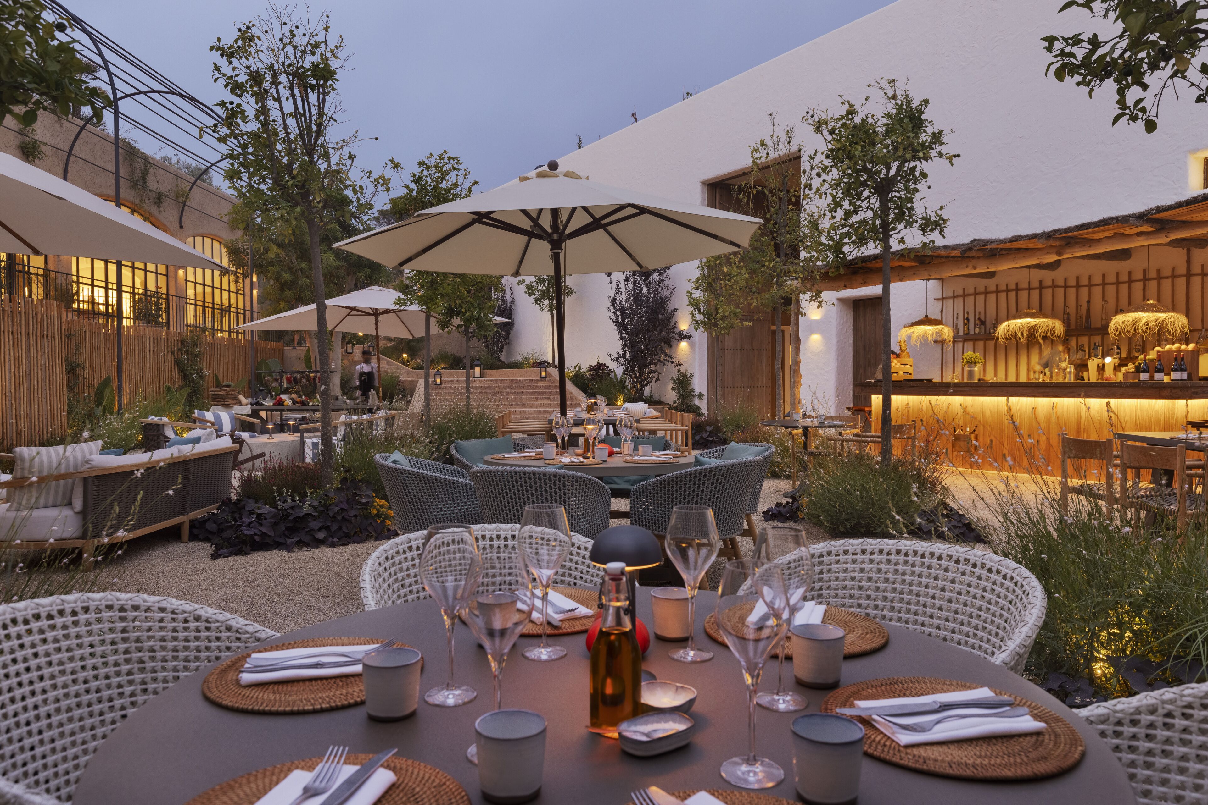 An outdoor dining area with wicker furniture, round tables, and umbrellas.
