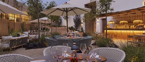 An outdoor dining area with wicker furniture, round tables, and umbrellas.