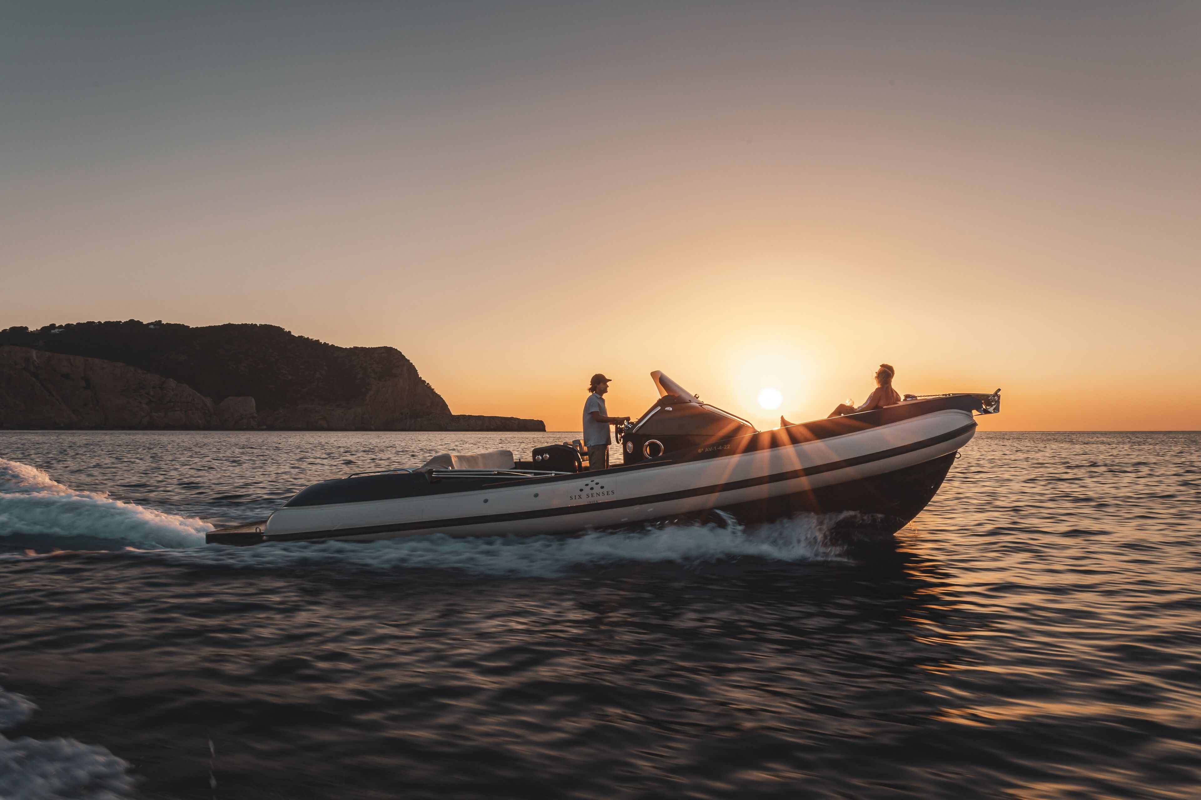 Un bateau à moteur sur l’eau, avec un coucher de soleil en arrière-plan.
