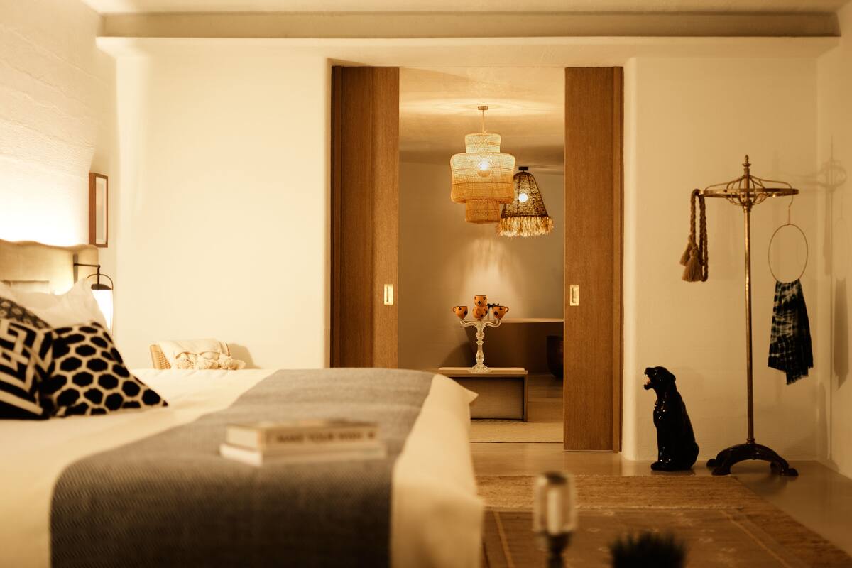 Een hotelkamer met een bed, een nachtkastje met een boek, een hanglamp en een kapstok met een jas.