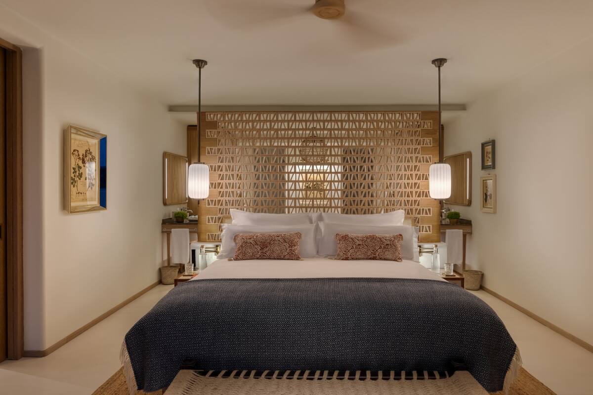 Een moderne hotelkamer met een groot bed, twee nachtkastjes, een houten hoofdbord en hanglampen.