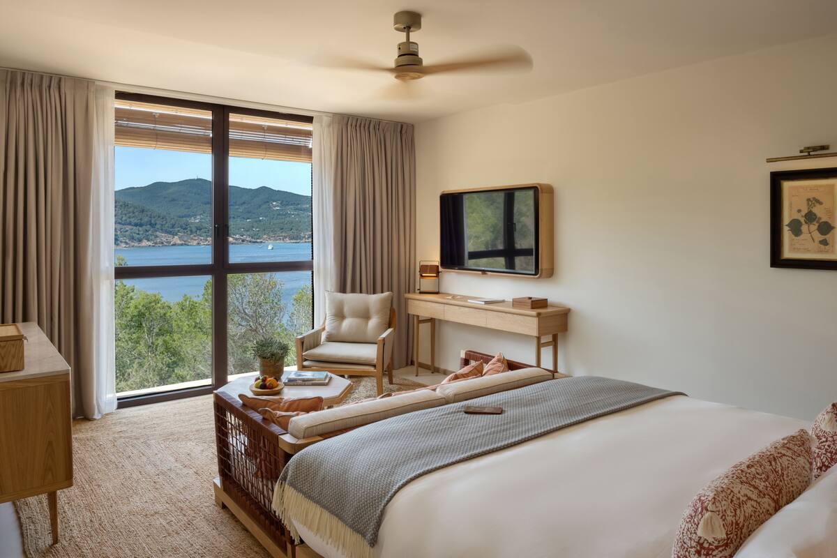 Een slaapkamer met een groot bed, een bureau, een stoel en uitzicht op zee.