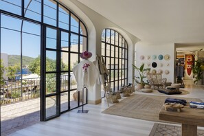 A spacious room with large windows, a variety of hats on the wall, and a cozy seating area with a rug and cushions.