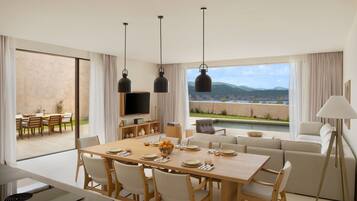 Un comedor moderno con una mesa grande, sillas y un televisor. Se ve un sofá y una lámpara al fondo.