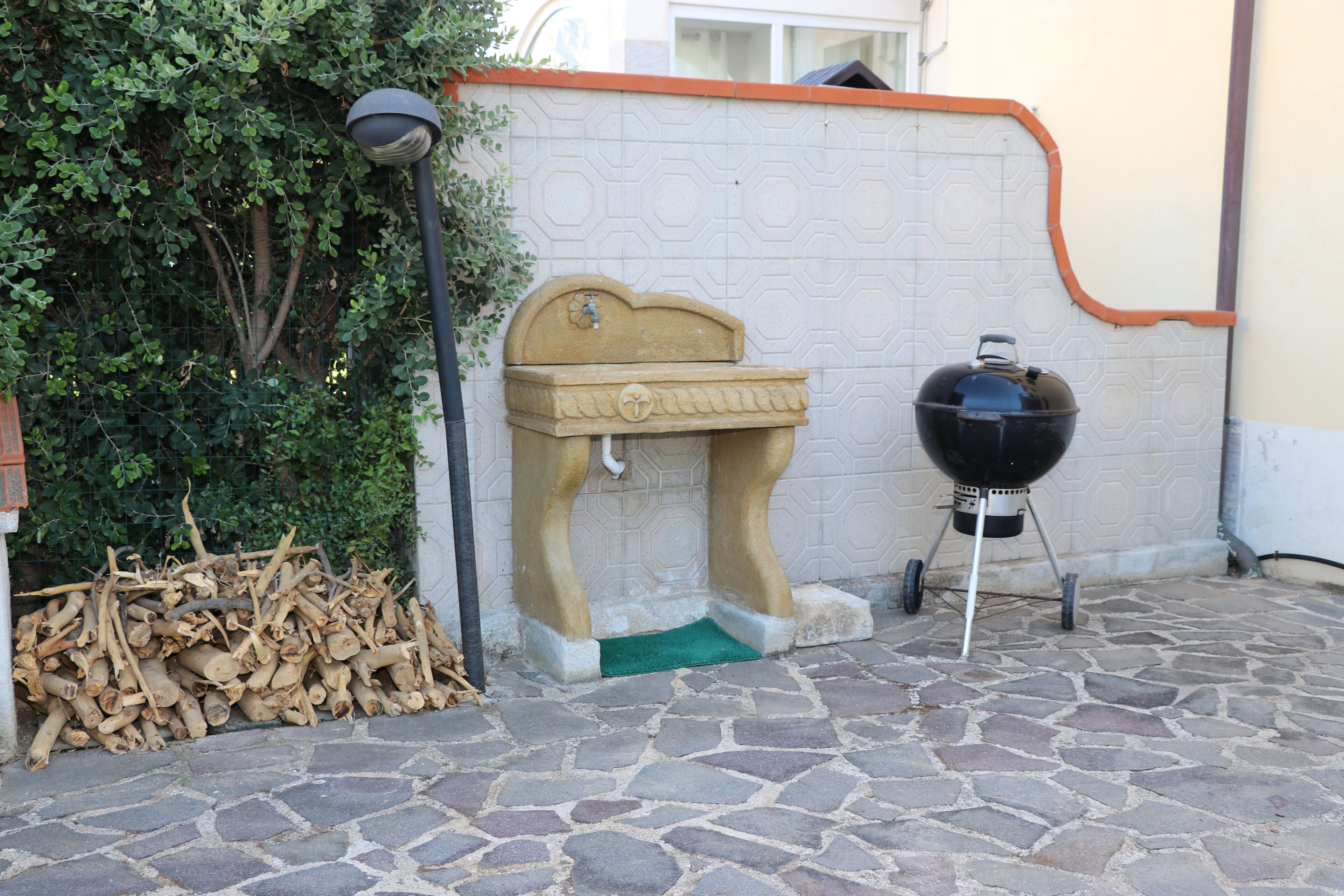 A stone patio with a barbecue grill and a decorative stone fountain.