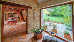 A rustic stone interior with a dining area, wooden staircase, and a view of a lush garden through large windows. - Charme et Tradition (trefumel)