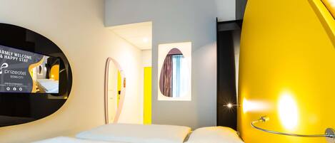 Een moderne hotelkamer met een bed, een spiegel en een geel accentmuur.