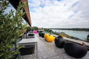 A terrace with outdoor seating, a river view, and a patterned floor. - Prize by Radisson, Bonn City (Bonn)