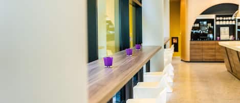 A modern interior with a wooden counter and white chairs along a windowed wall.