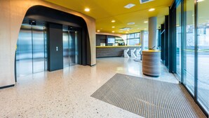 A modern lobby with a speckled floor, a reception desk, and a glass wall offering a view outside. - Prize by Radisson, Bonn City (Bonn)