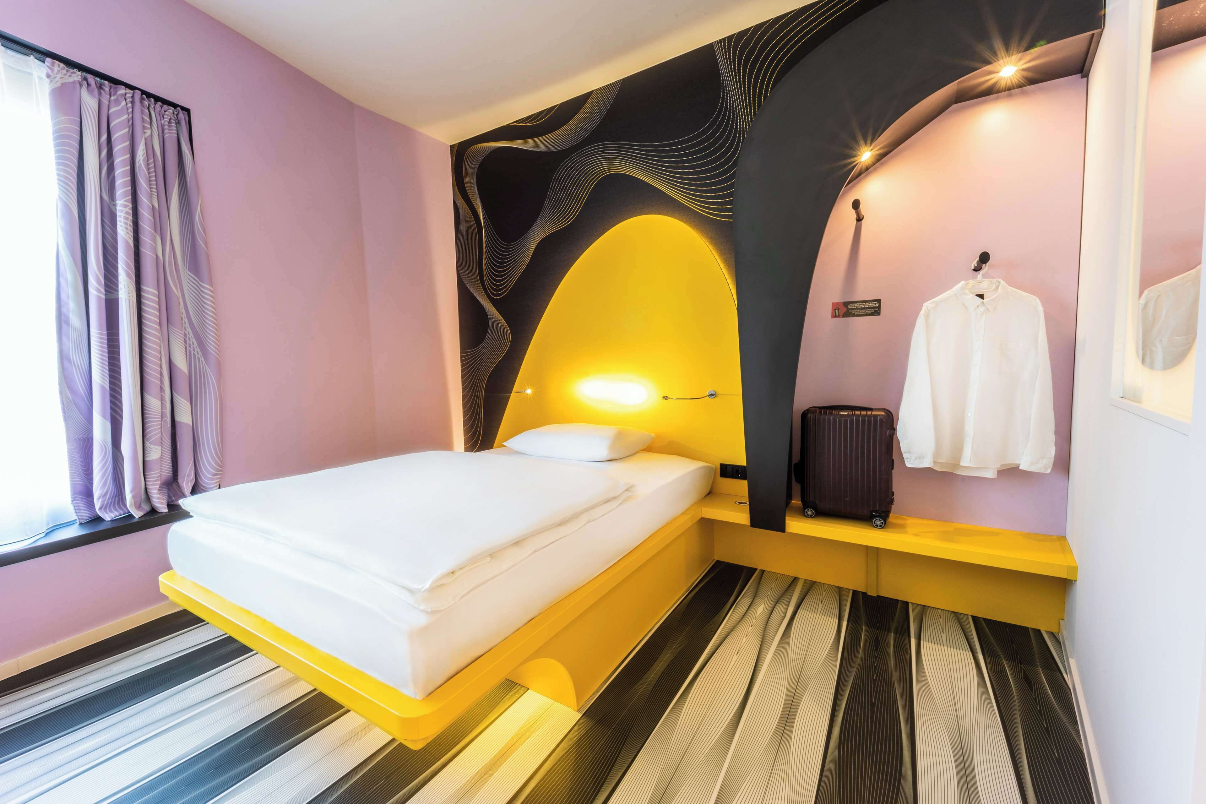 Une chambre d’hôtel moderne avec un lit, une valise et un porte-manteau.