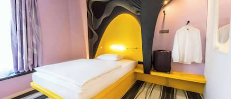 Una habitación de hotel moderna con una cama, una maleta y un perchero.