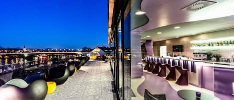 A modern bar area with a panoramic view of the cityscape at dusk.