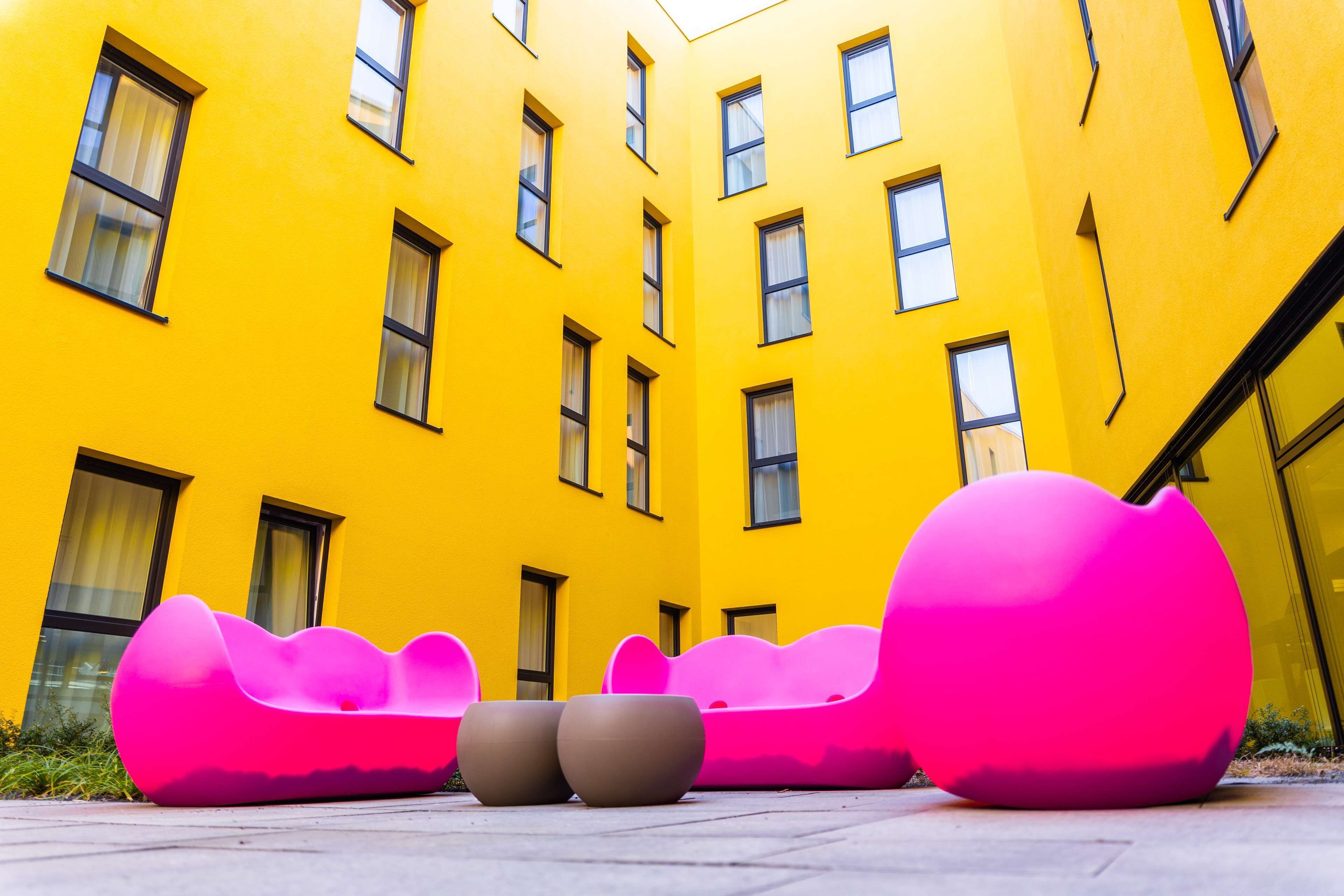 A yellow building with multiple windows and a courtyard with pink and brown seating.