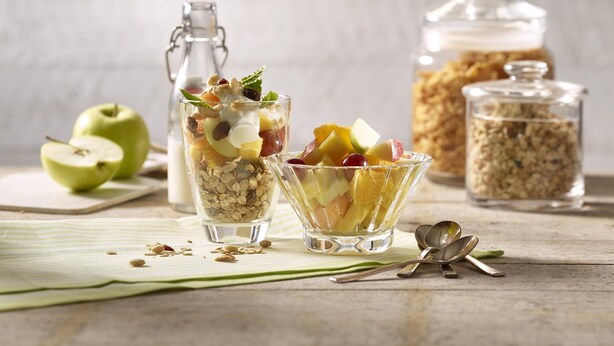 Two glasses of fruit salad with a bottle and jars of granola in the background. - Premier Inn Wiesbaden City Centre (Wiesbaden)