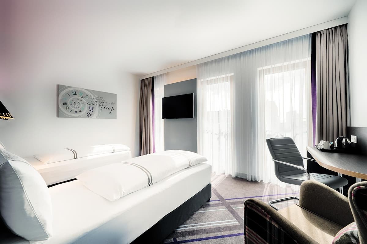 A modern hotel room with a bed, a desk, a chair, and a TV.