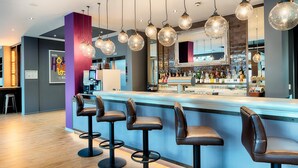 Zona de bar con taburetes, lámparas colgantes y barra con botellas.