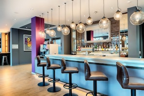 A bar area with stools, hanging light fixtures, and a bar counter with bottles.