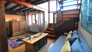 A cozy living room with a wooden staircase, a sofa, a wooden table, and a patterned rug.