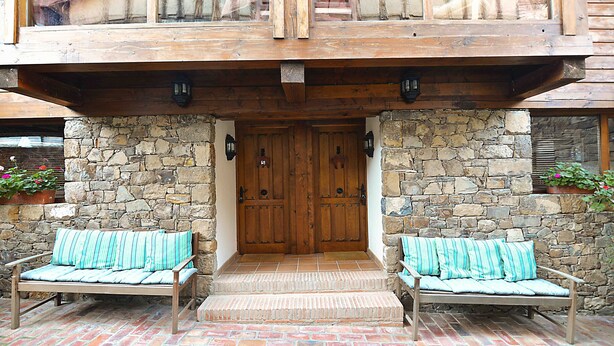 A wooden entrance with a stone wall, two benches with striped cushions, and a wooden door.