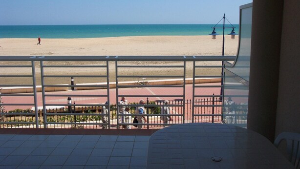 A balcony with a view of a beach and a pedestrian walkway.
