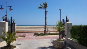 A paved pathway leading to a beach with palm trees and a fence.