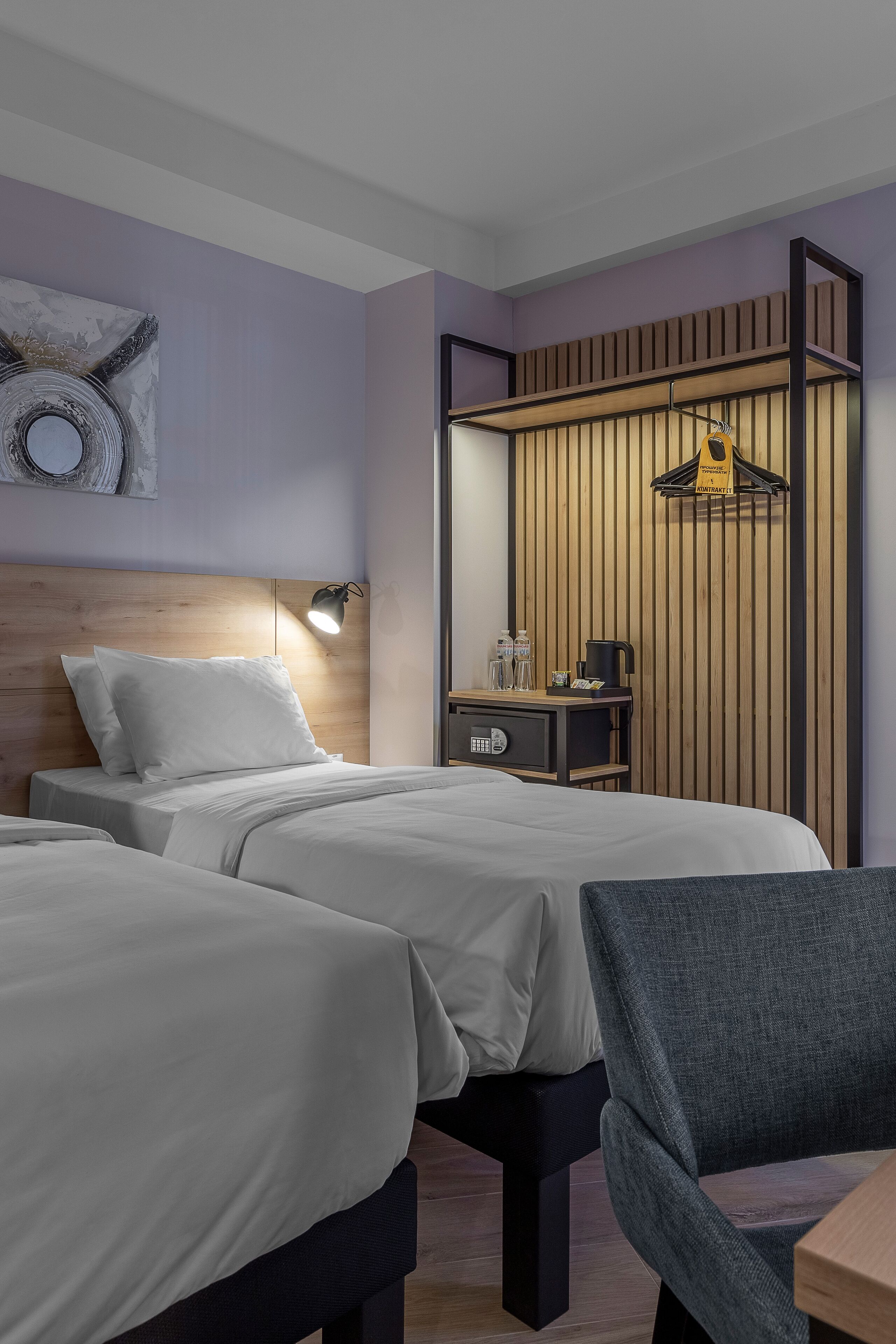 Una habitació d'hotel amb dos llits, un panell de capçalera de fusta, una taula de nit amb una làmpada, un mirall i una petita estant amb productes de tocador.