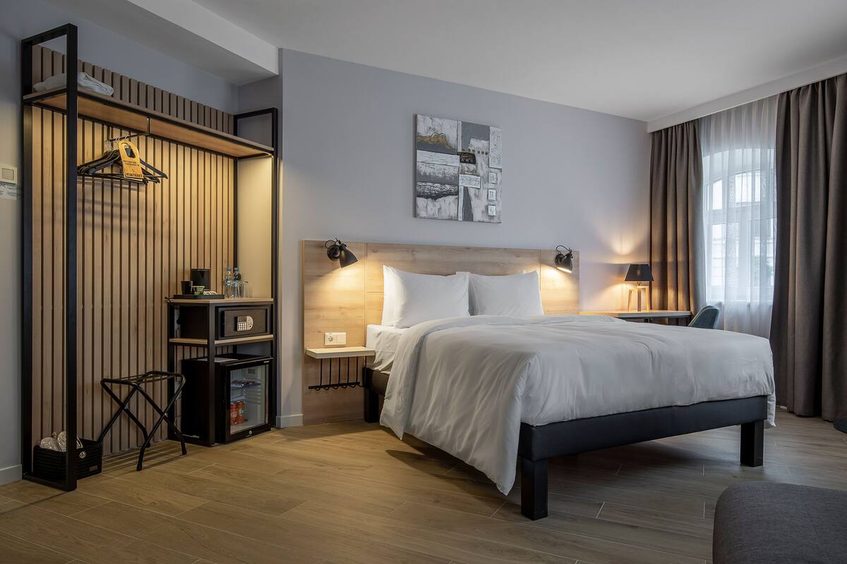 A modern hotel room with a bed, bedside tables, a wardrobe, and a painting on the wall.