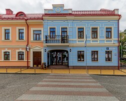 A row of colorful buildings with a central entrance, a signboard, and a visible street name.