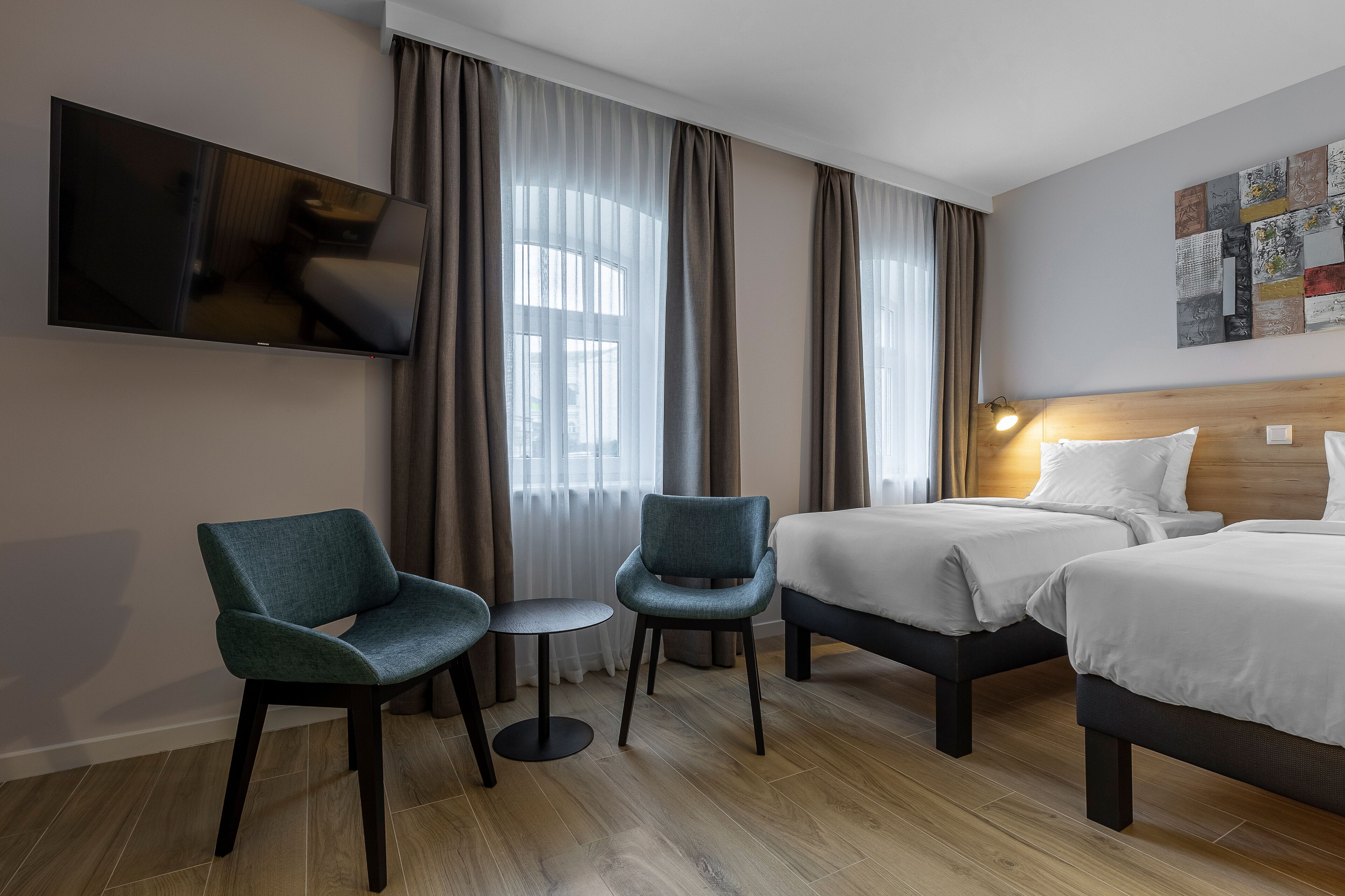 A hotel room with two beds, a TV mounted on the wall, a small round table, and a chair.