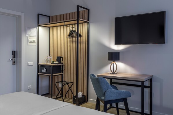A hotel room with a bed, a desk with a chair, a TV mounted on the wall, a wardrobe, and a small table with a lamp. - KONTRAKT Boutique Hotel (Kyiv)