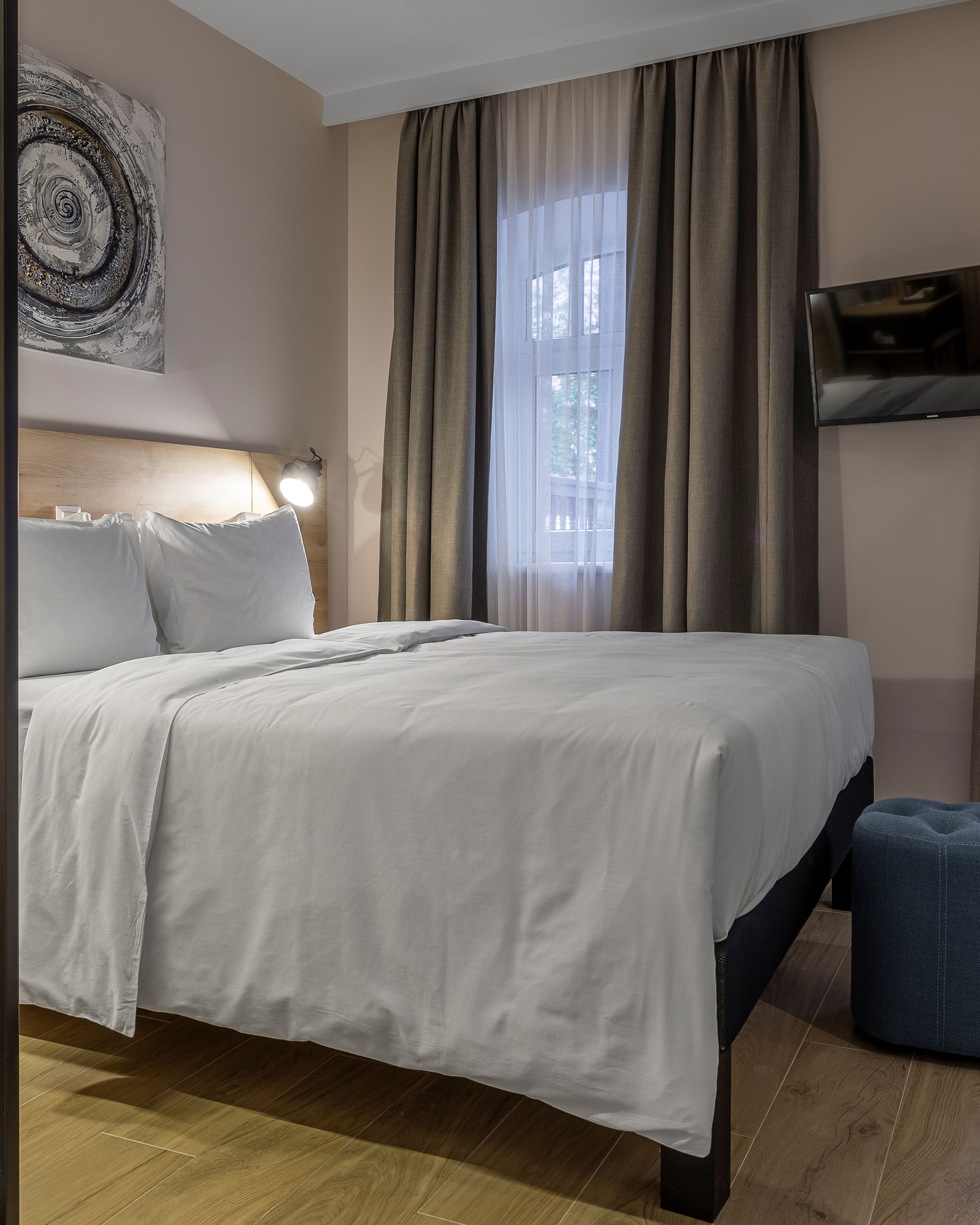 A hotel room with a bed, a TV mounted on the wall, and a window with curtains.