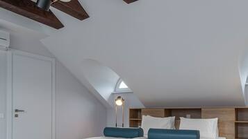 A modern bedroom with a sloped ceiling, a skylight, a bed with white bedding and blue pillows, and a floor lamp.