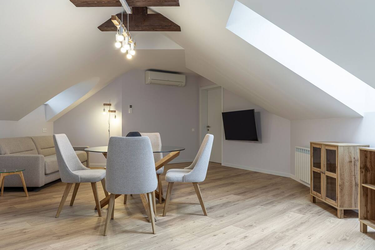 A modern loft apartment with a dining area, a sofa, and a TV mounted on the wall.