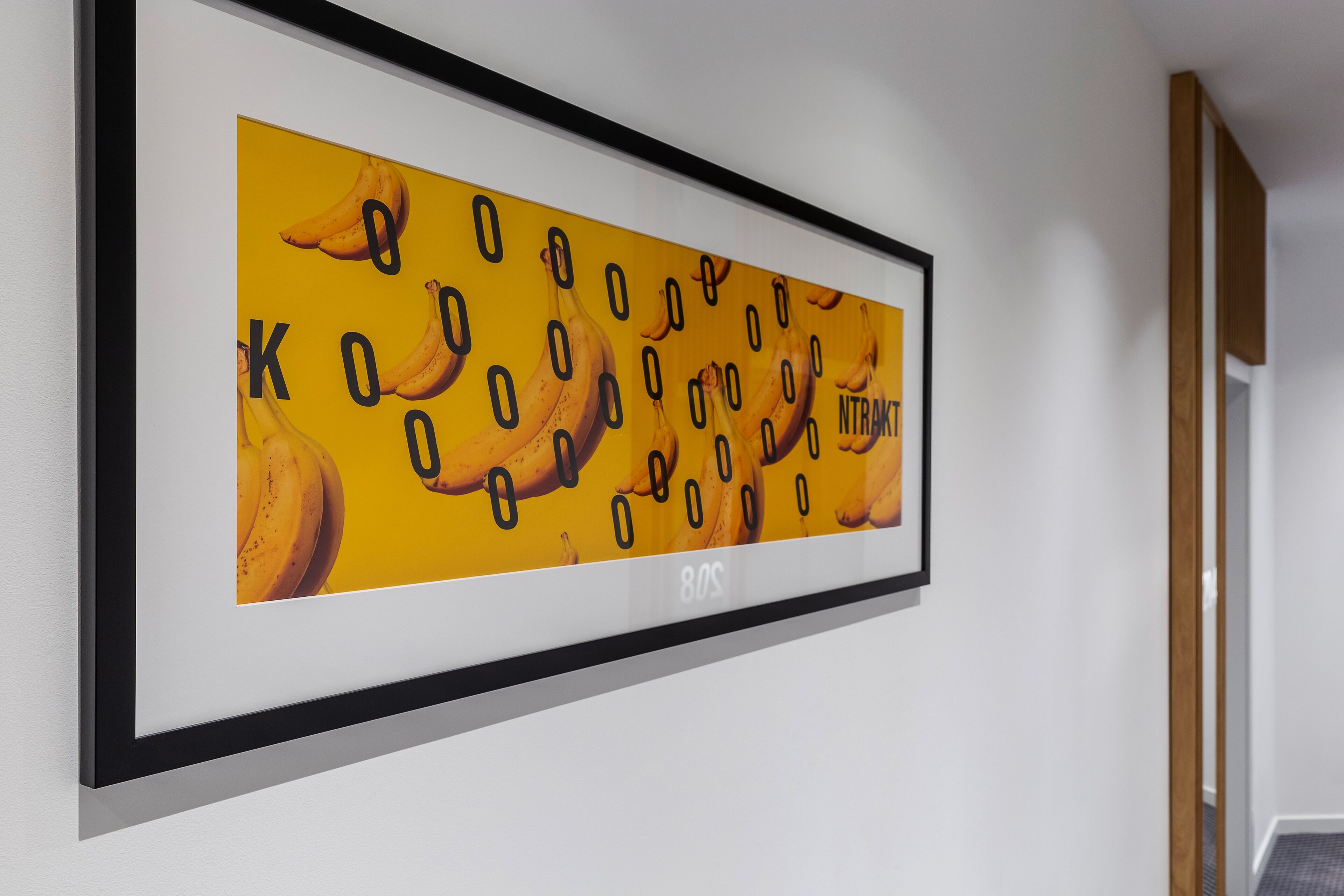 A framed artwork with bananas and numbers on a white wall.