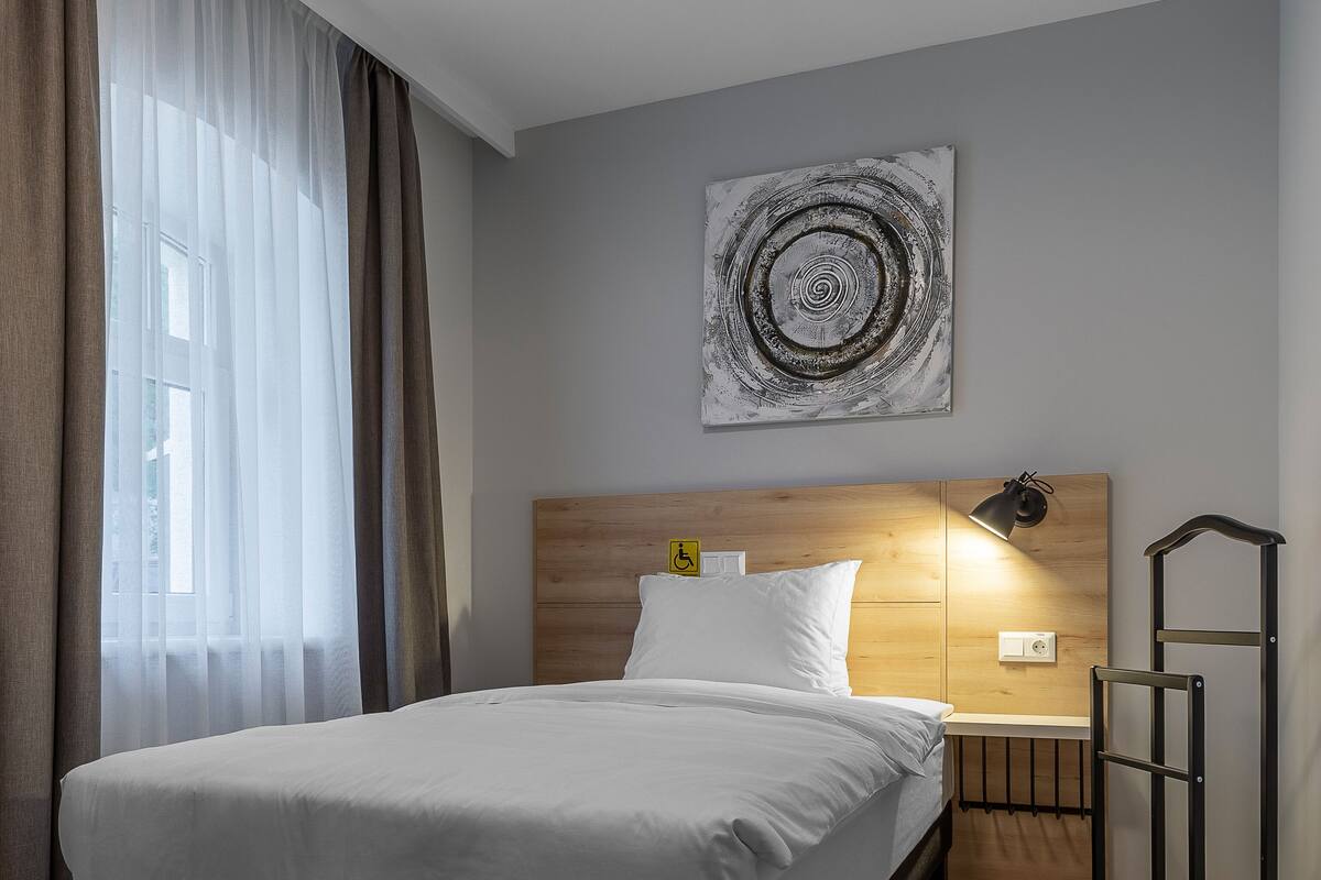 A modern hotel room with a large bed, wooden headboard, and a bedside table with a lamp.