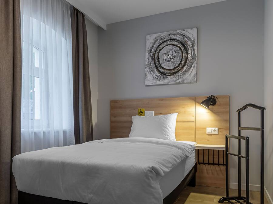 Ein modernes Hotelzimmer mit einem großen Bett, einem Holzkopfteil und einem Nachttisch mit Lampe.