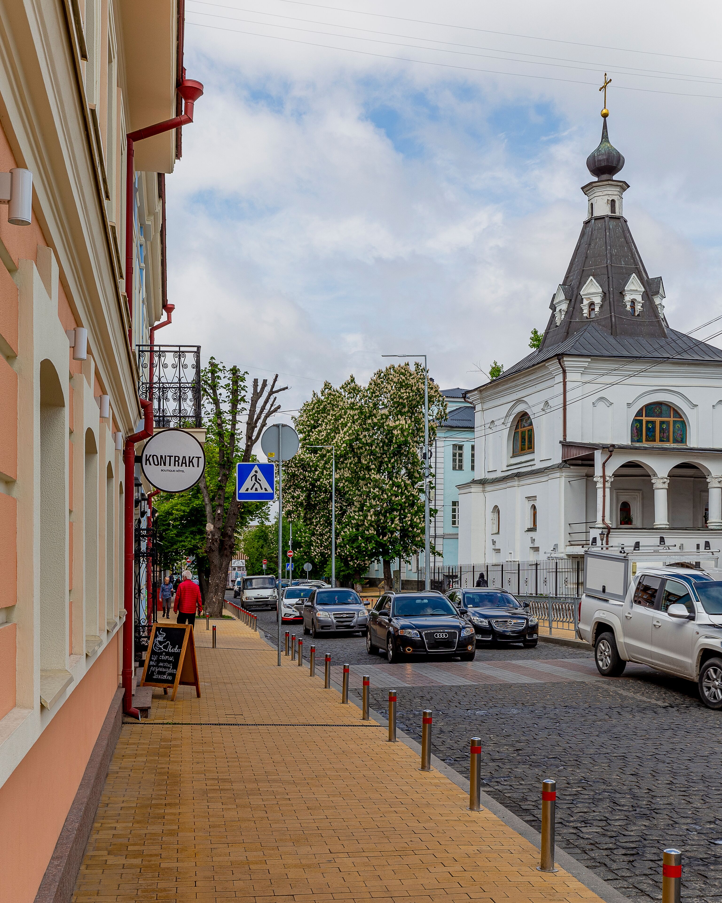 A cobblestone street with a hotel named "Kontrakt Boutique Hotel" on the left.